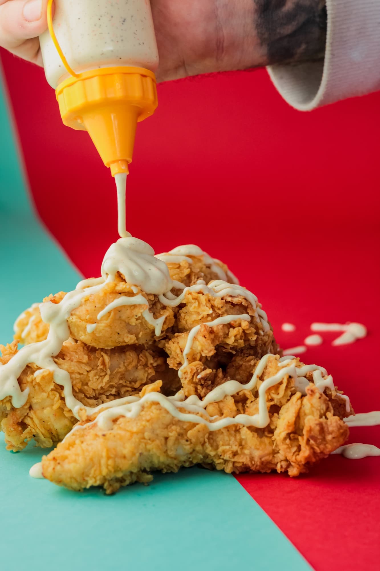 Pilha de frango frito crocante recebendo um fio de molho cremoso