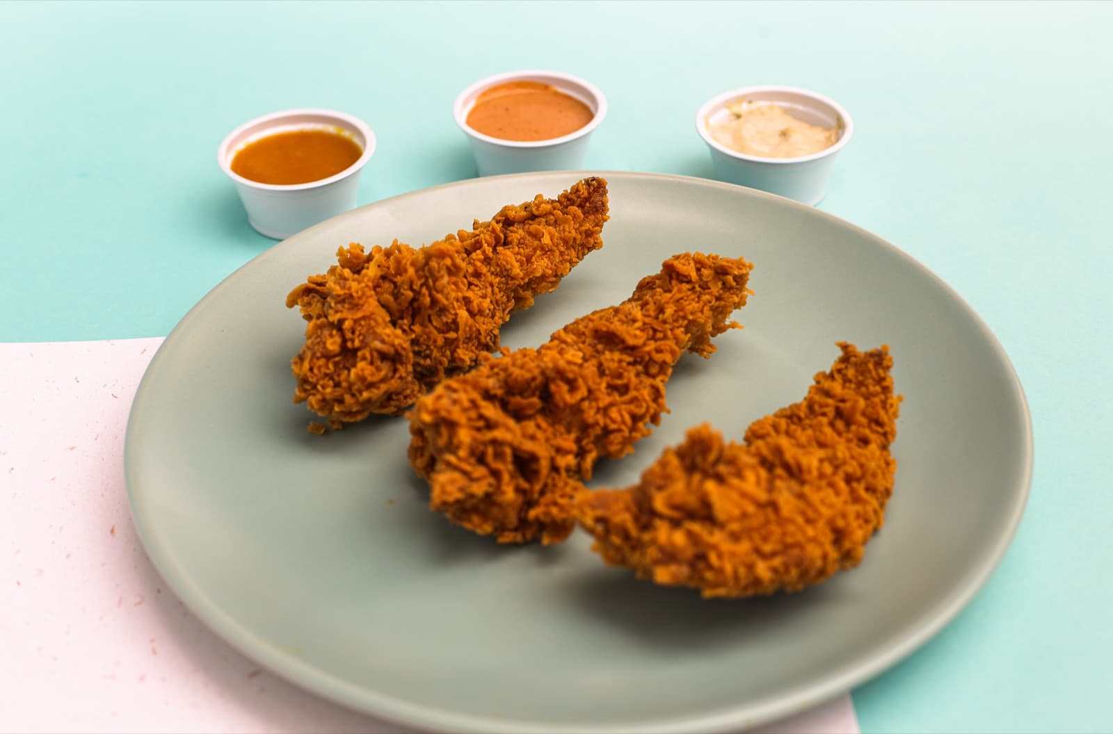 Prato com tiras de frango frito crocante e três potes de molhos